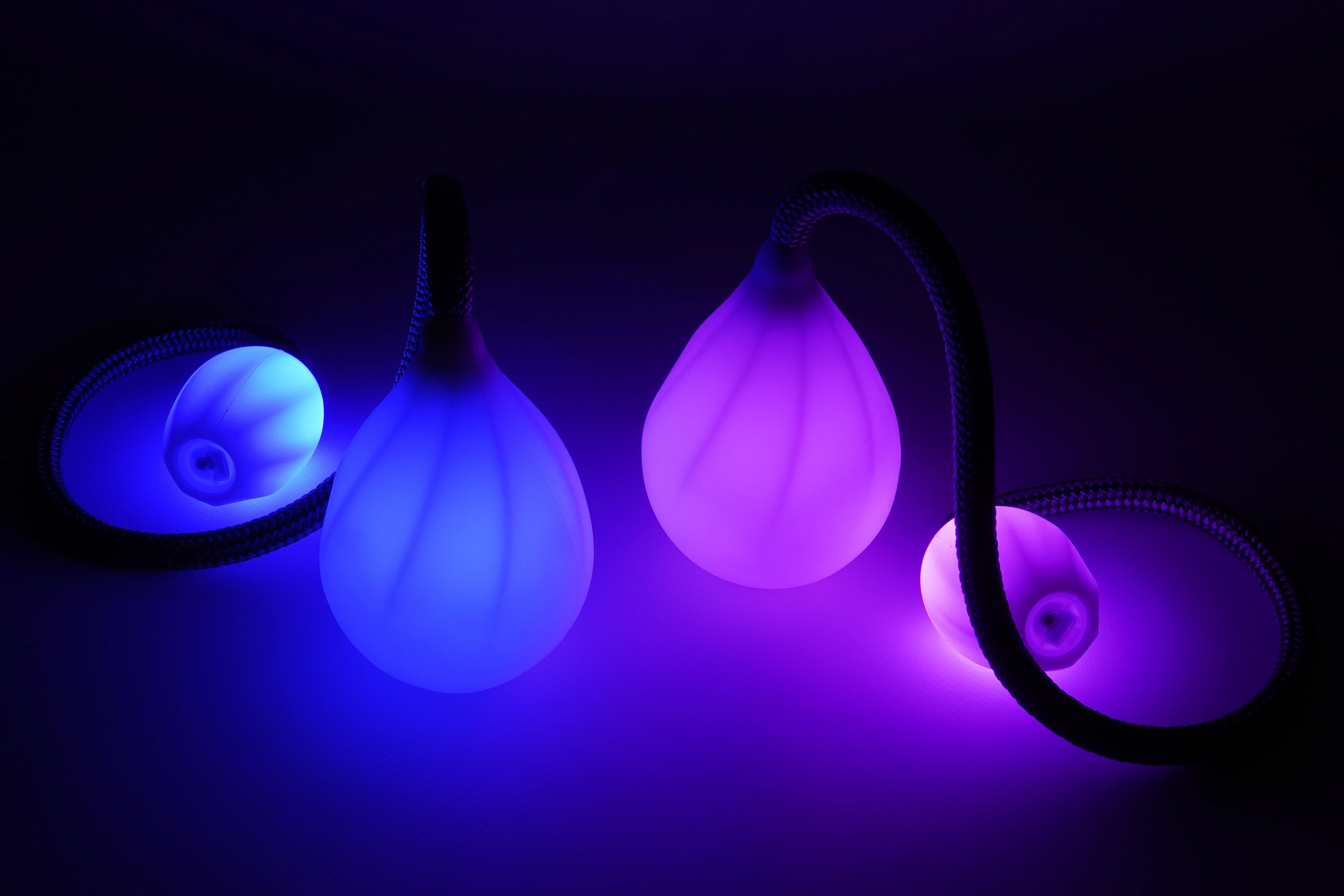 A pair of Lumi Advanced LED Poi with glowing handles in a dimly lit environment, displaying multiple colors.